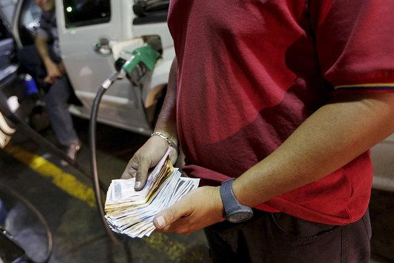 Бензин в Венесуэле был и остается самым дешевым в мире, несмотря на повышение цены литра 95-го более чем на 6000%. Работники АЗС порой получают от водителей больше чаевых за помощь в заправке, чем кассир – за наполнение бака. На фото: заправщик считает деньги на АЗС госкомпании PdVSA